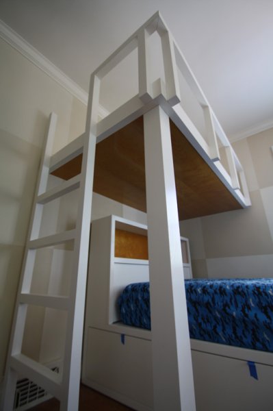 Bunk bed has a double mattress below with a transverse-mounted single above. Base has drawers and cabinets. Ladder and railings are solid ash.